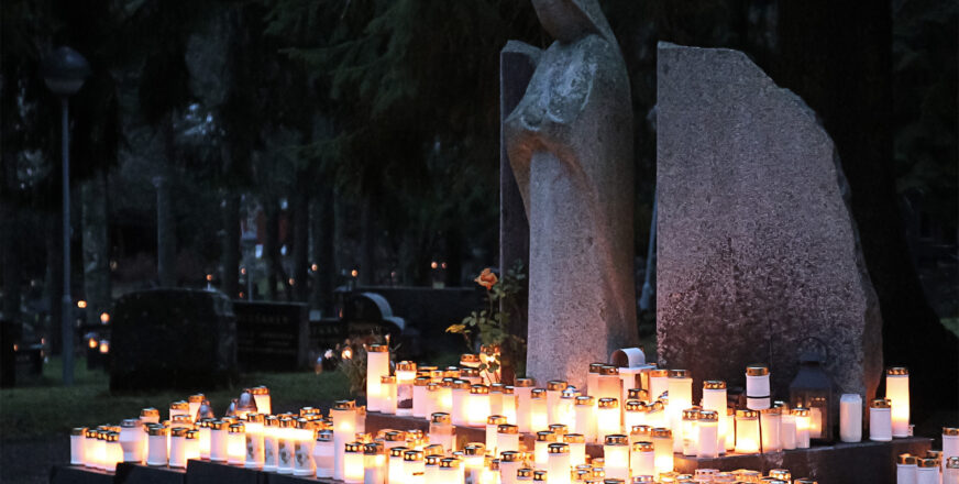 pimeällä hautausmaalla loistaa kynttilöitä, enkelipatsaan juurella kynttilämeri