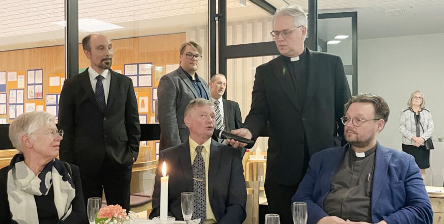 Kirkkoherra Matti Pentikäinen pitää mikrofonia puhujalle kahvitilaisuudessa.