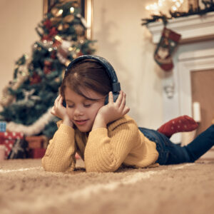 Lapsi lattialla kuulokkeet päässään, taustalla joulukuuri.