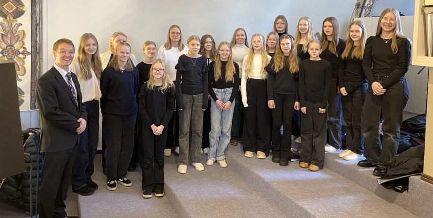 Nuorisokuorolaiset eli ryhmä tyttöjä ja kuoronjohtaja Vesa Kajava seisovat Siilinjärven kirkon parvella