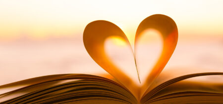Kirja auki, käännetyt sivut muodostavat sydämen sivuprofiilin. Kirjan takana auringonlasku.