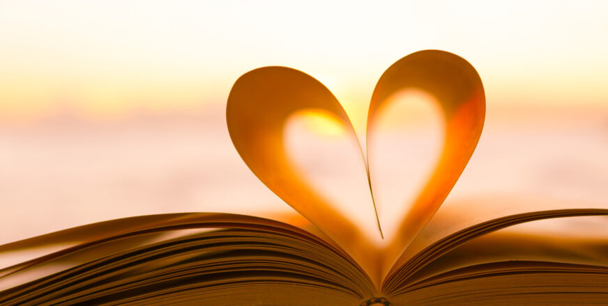 Kirja auki, käännetyt sivut muodostavat sydämen sivuprofiilin. Kirjan takana auringonlasku.