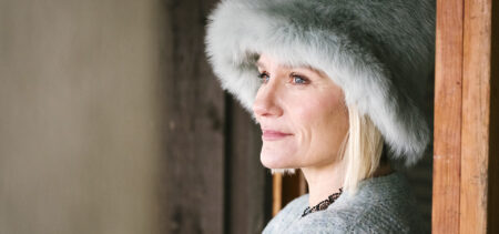 Laura Malmivaara katsoo kameraan ja hymyilee. Päässään hänellä on harmaa pörröinen hattu.