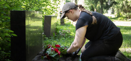 Ihminen istuttaa kukkaa haudalle.