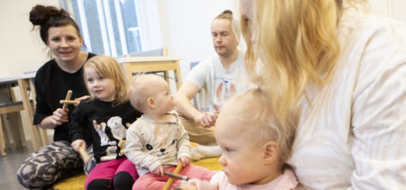 Aikuisia ja pikkulapsia lattialla, käsissä rytmikapulat.