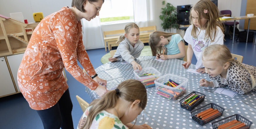 Ohjaaja ja leiriläiset askartelevat kesispasseja.