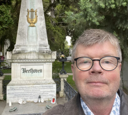 Mies seisoo Beethovenin hautakiven edessä, poseeraa kameralle.