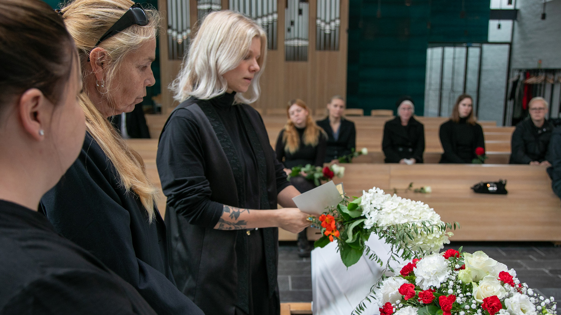 Nainen lukee arkun äärellä kortista muistokirjoitusta.