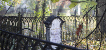 Hautakivi ruostuneen aidan sisäpuolella, syksyisessä sumuisessa aamussa.