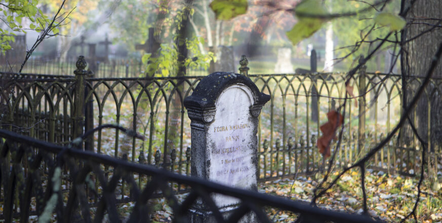 Hautakivi ruostuneen aidan sisäpuolella, syksyisessä sumuisessa aamussa.