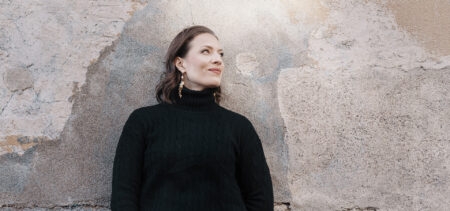 Ida Elina nojaa kiviseinään ja katsoo sivulle hymyillen.