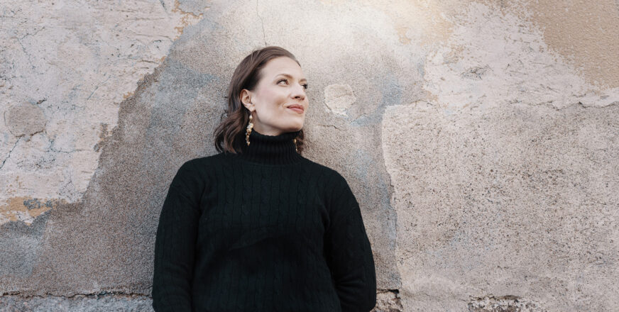 Ida Elina nojaa kiviseinään ja katsoo sivulle hymyillen.