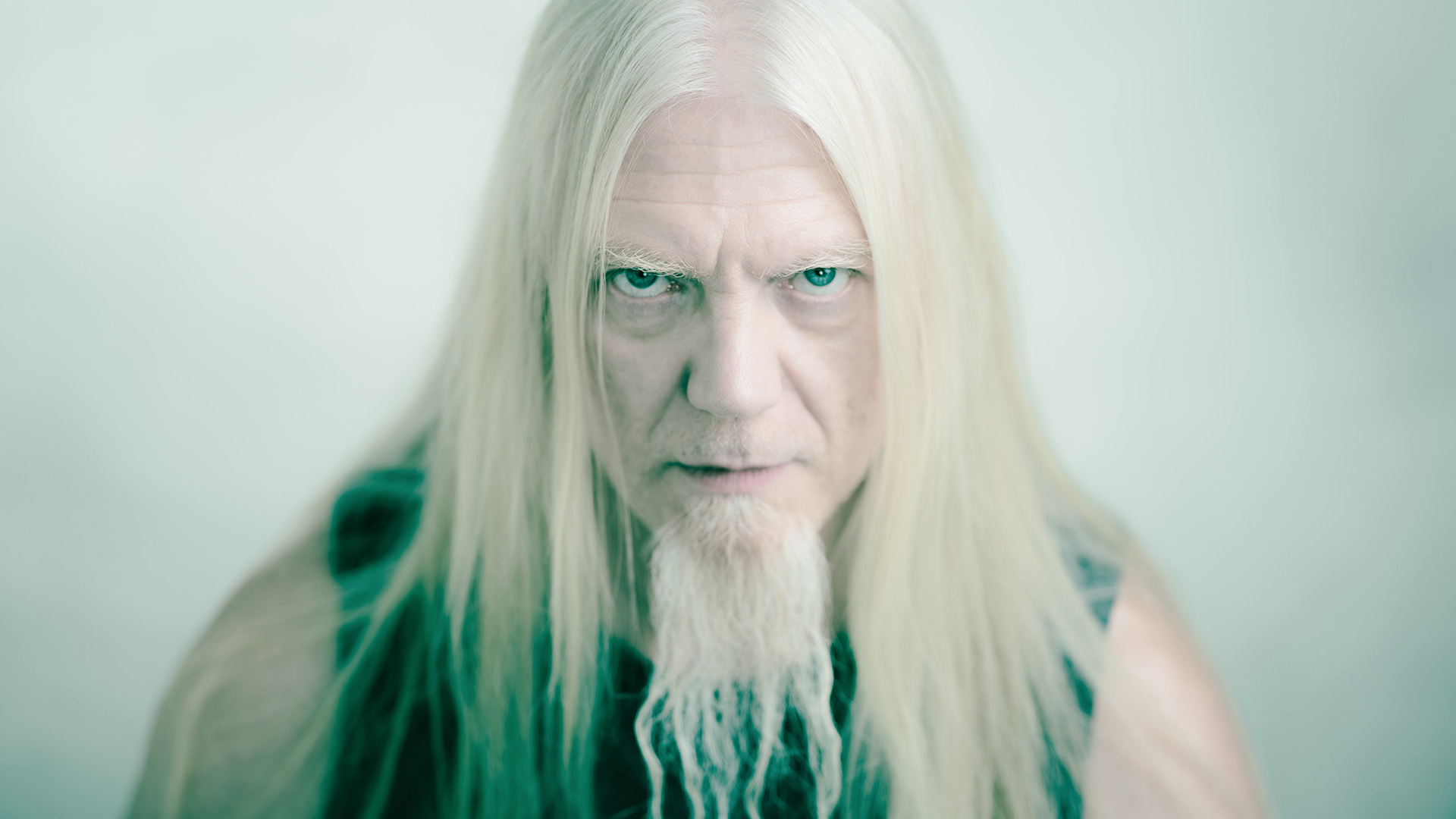 Marko Hietala kasvokuvassa, katsoo kameraan alta kulmien, vaaleat pitkät hiukset valuvat olkapäille, pitkä parta