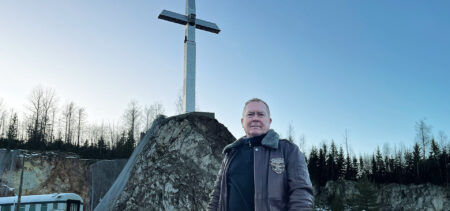 Matti Kuosmanen taustallaan kallion päällä seisova suuri risti.