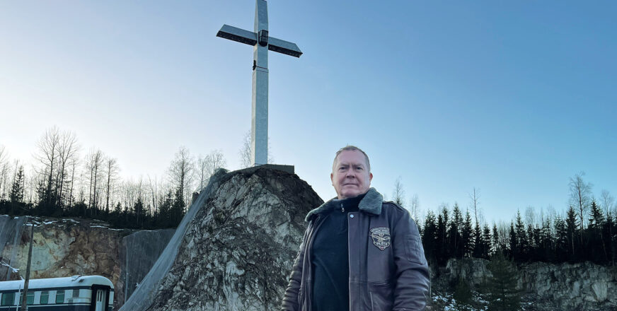 Matti Kuosmanen taustallaan kallion päällä seisova suuri risti.