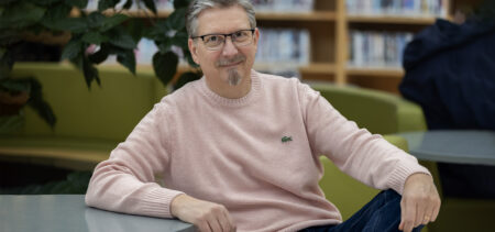 Kirjailija Tatu Kokko nojaa rennosti pöytään kirjastossa.