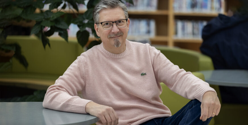 Kirjailija Tatu Kokko nojaa rennosti pöytään kirjastossa.