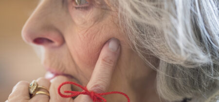 Lähikuva iäkkäästä naisesta, jonka etusormeen on sidottu rusetille punainen lanka.