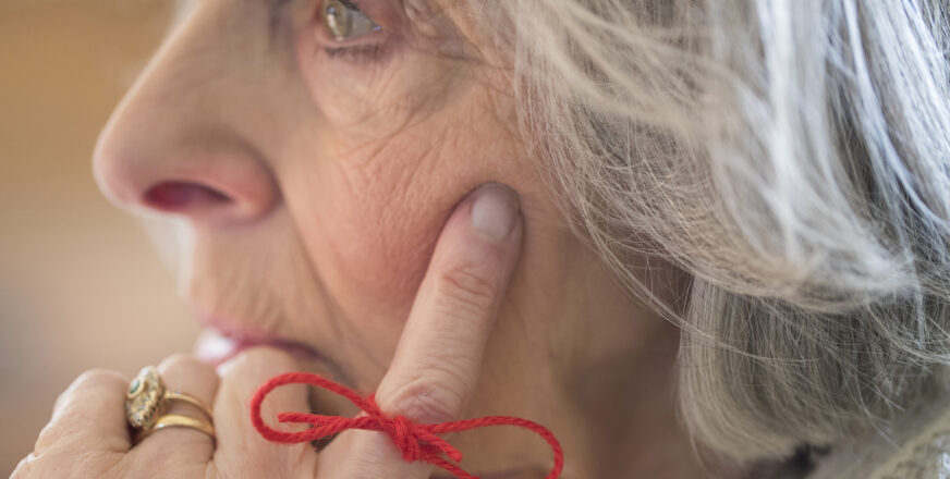 Lähikuva iäkkäästä naisesta, jonka etusormeen on sidottu rusetille punainen lanka.