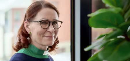 Liisa Tiilikainen katsoo hymyillen kameraan. Hänellä on yllään vihreä diakoniatyöntekijän pantapaita.