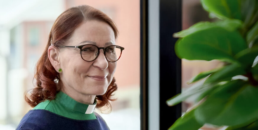 Liisa Tiilikainen katsoo hymyillen kameraan. Hänellä on yllään vihreä diakoniatyöntekijän pantapaita.