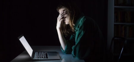 Nuori istuu pimeässä huoneessa ja nojaa väsyneenä ja ahdistuneena käteensä, edessä valkoisena loistaa tietokoneen ruutu.