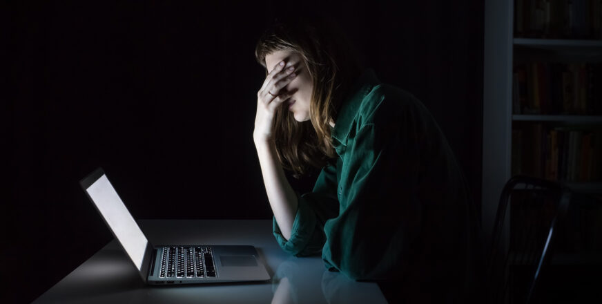 Nuori istuu pimeässä huoneessa ja nojaa väsyneenä ja ahdistuneena käteensä, edessä valkoisena loistaa tietokoneen ruutu.
