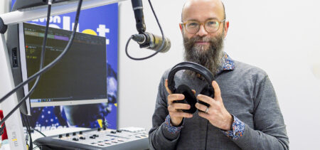 Anssi Saarelainen seisoo radiostudiossa mikin edessä kuulokkeet kädessään.