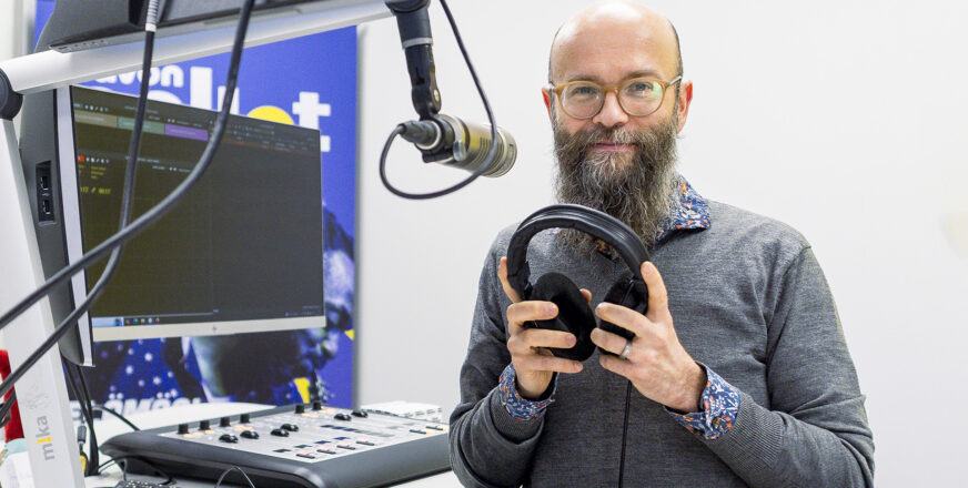 Anssi Saarelainen seisoo radiostudiossa mikin edessä kuulokkeet kädessään.