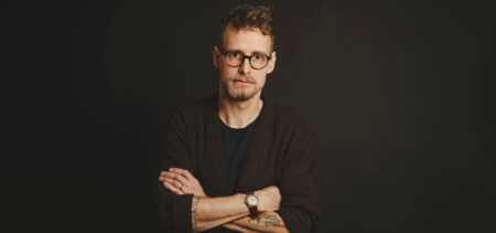 Lari Launonen katsoo kädet puuskassa suoraan kameraan. Hänellä on musta paita ja myös tausta on musta.