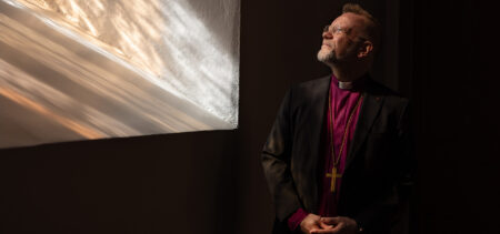 Piispa Jari Jolkkonen kohottaa katseensa kohti kirkon ikkunaa, josta tulee auringonsäteitä.