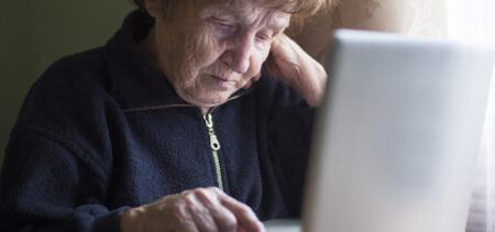 Iäkäs nainen näppäilee kannettavan tietokoneen näppäimiä.