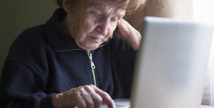 Iäkäs nainen näppäilee kannettavan tietokoneen näppäimiä.