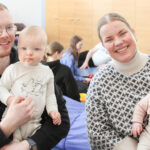 Kaksi vanhempaa istuu lattialla lapset sylissään iloisina.