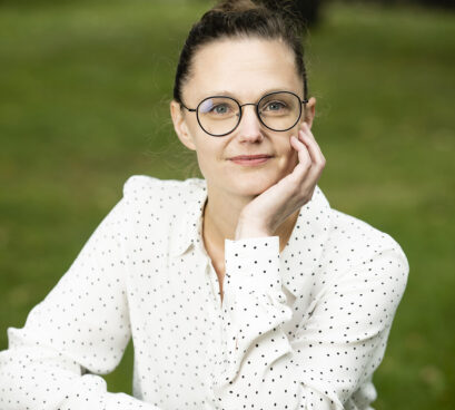 Henkilö katsoo hymyillen kohti kameraa ja nojaa kädellä poskeensa.