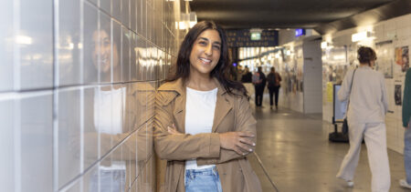 Amani Al-mehsen nojaa asematunnelin seinään ja hymyilee, tunnelissa kulkee ihmisiä.