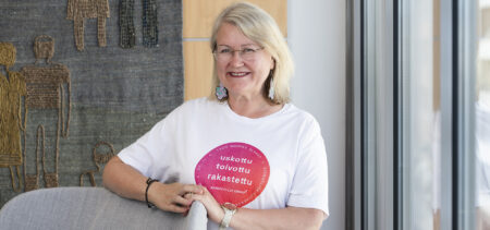 Annmari Salmela seisoo hymyillen nojatuolin takana käsi tuolin selkänojalla.